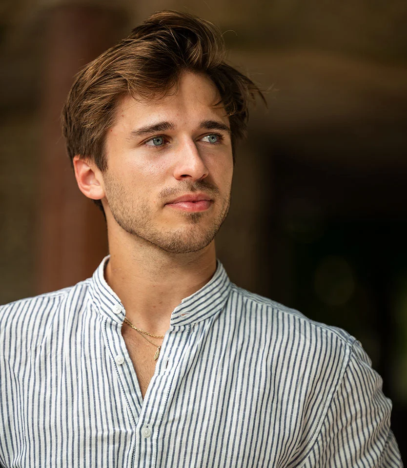Young man with styled hair and light facial stubble looking off to the side in a striped shirt - FUT Hair Transplant in New York, NY