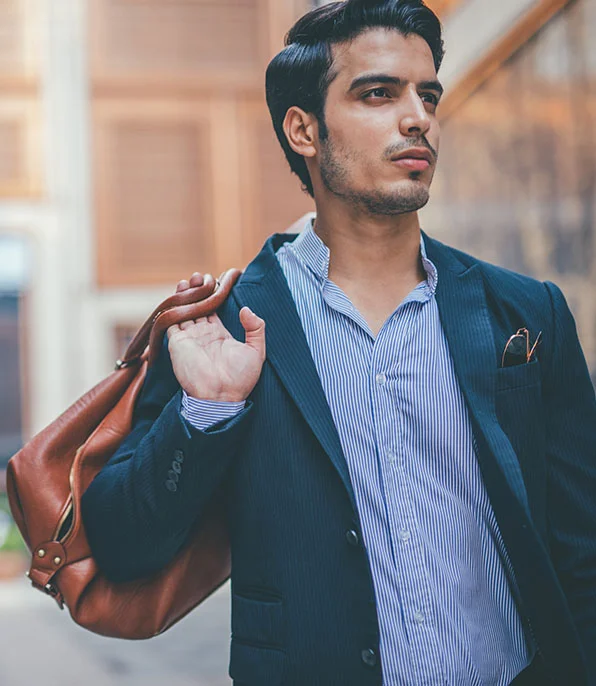 Man in a blazer carrying a brown leather bag over his shoulder while walking through the city - Out of Town Patient Resources in New York, NY