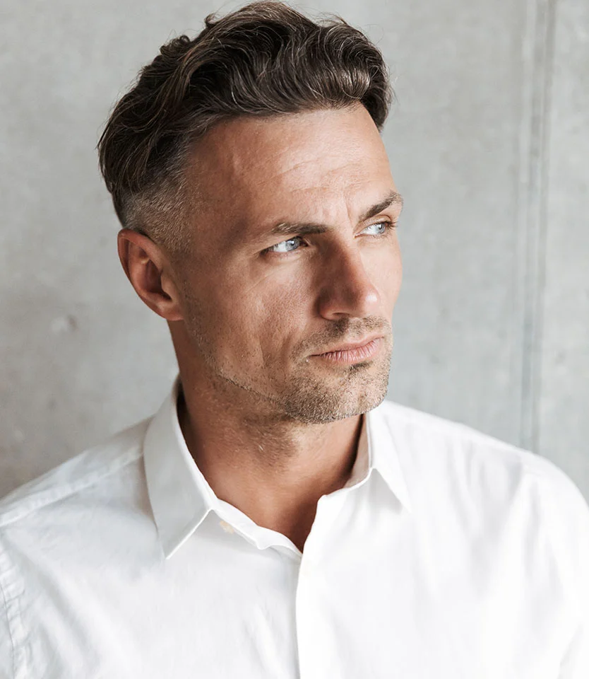 Man with styled hair and light stubble looking off to the side in a white shirt - Robotics Transplant ARTAS in New York, NY