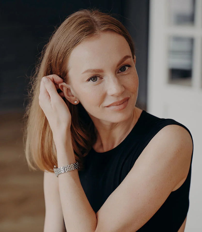 Woman touching her hair and smiling softly while sitting indoors - Types of Hairloss in New York, NY